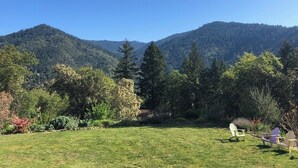 Ein grünes Feld mit zwei Adirondack-Stühlen, einem Haus im Hintergrund und einem bewaldeten Gebirgszug.