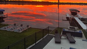 Een uitzicht op het water met een zonsondergang, een steiger, lounge stoelen en een zwembad.