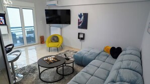 Un salon moderne avec un canapé, un fauteuil jaune, un téléviseur à écran plat et un jeu d’échecs.
