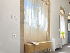 A room with a stone wall, a wicker bench, a radiator, and a window with sheer curtains. - Vineyard View, next to Best Wineries, "Theros" appartment (52QJ+W6 Avgeniki)