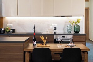 A modern kitchen with a marble countertop, wooden cabinets, and a dining area with a table and chairs. - Vineyard View, next to Best Wineries, "Theros" appartment (52QJ+W6 Avgeniki)