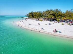 A beach with white sand, clear turquoise water, and a row of parked cars along the shore. - Longboat Key Modern Beach House Gem (Longboat Key)
