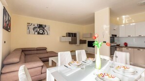 Ein modernes Wohnzimmer mit einer Couch, einem Esstisch für vier Personen und einer Küche im Hintergrund.