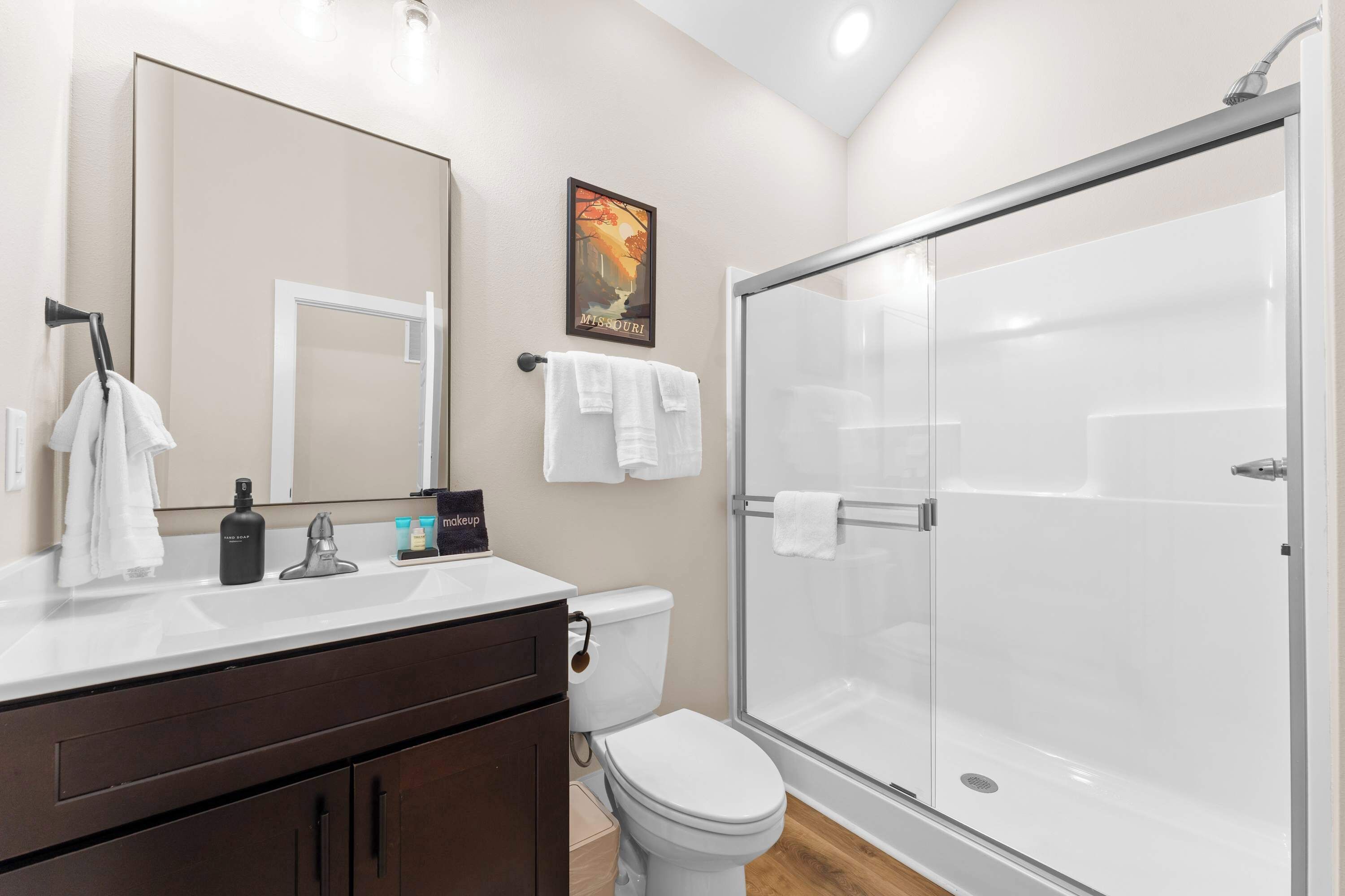 A modern bathroom with a glass shower enclosure, a white toilet, and a vanity with a mirror and towel rack.