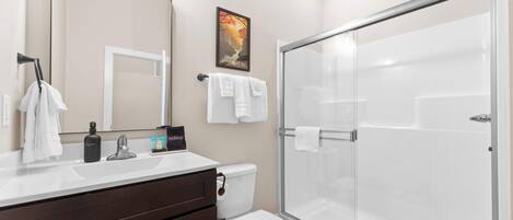 A modern bathroom with a glass shower enclosure, a white toilet, and a vanity with a mirror and towel rack.