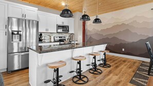 Una cocina moderna con un refrigerador de acero inoxidable, un microondas y una isla de madera con taburetes de bar.