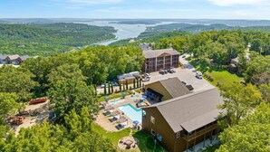 Un albergue con piscina, mobiliario exterior y vistas a un lago y bosque.