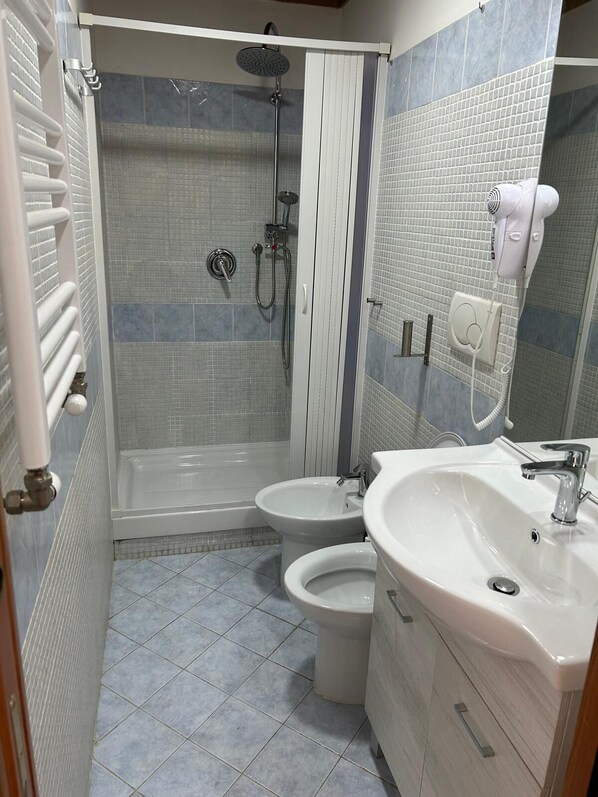 A bathroom with a shower, two toilets, a sink, and a hairdryer. - Villa Lanusei (Rome)