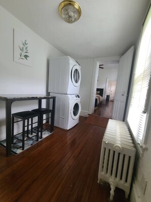 A laundry room with stacked washers and dryers, a radiator, and a wooden floor.