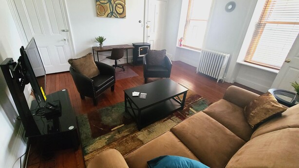 Una sala de estar con un sofá, una mesa de centro, un televisor, un escritorio y un radiador.