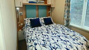 A bedroom with a bed, a nightstand, a dresser, a window with blinds, and a ceiling light. - 8 birth Diamond rated Caravan, en-suite, with decking, Parkdean, Skegness (Skegness)