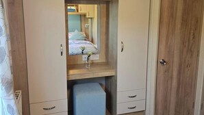 Een slaapkamer met een bed, een kledingkast, een spiegel en een klein krukje.