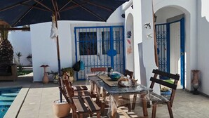 Une terrasse avec une table et des chaises, une piscine et un bâtiment blanc agrémenté de touches de bleu.