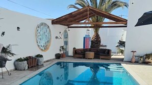 Une piscine aux eaux cristallines, dotée d’une terrasse en bois, de plantes en pot et d’un mur agrémenté d’éléments décoratifs.