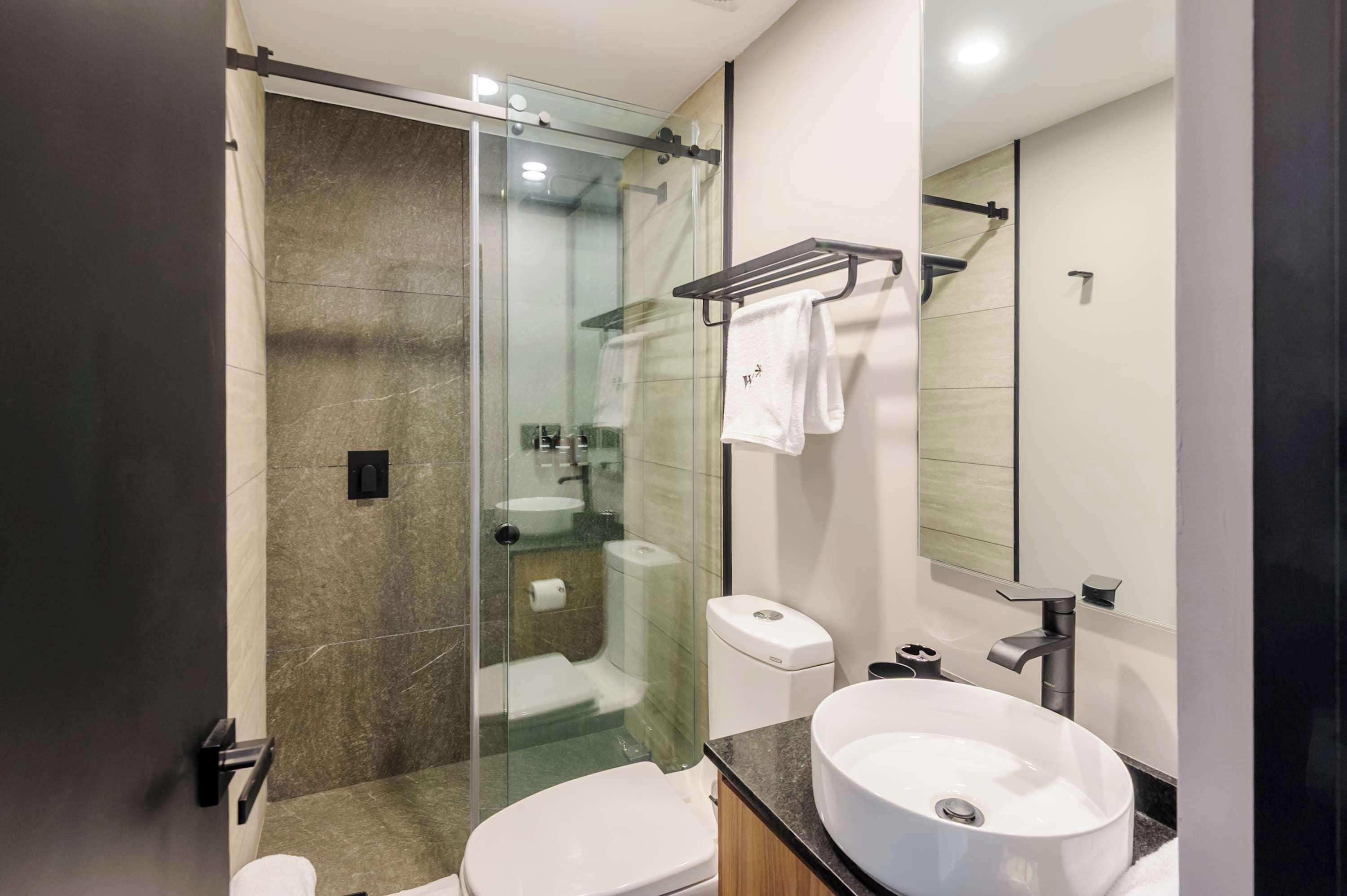 Un baño moderno con cabina de ducha de vidrio, un lavamanos blanco y un perchero para toallas.