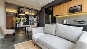 A modern living room with a sofa, dining table, chairs, and a kitchen area with wooden cabinets and appliances. - w* | Tasteful 1BR w/ Private Balcony in Tabacalera (Ciudad de México)