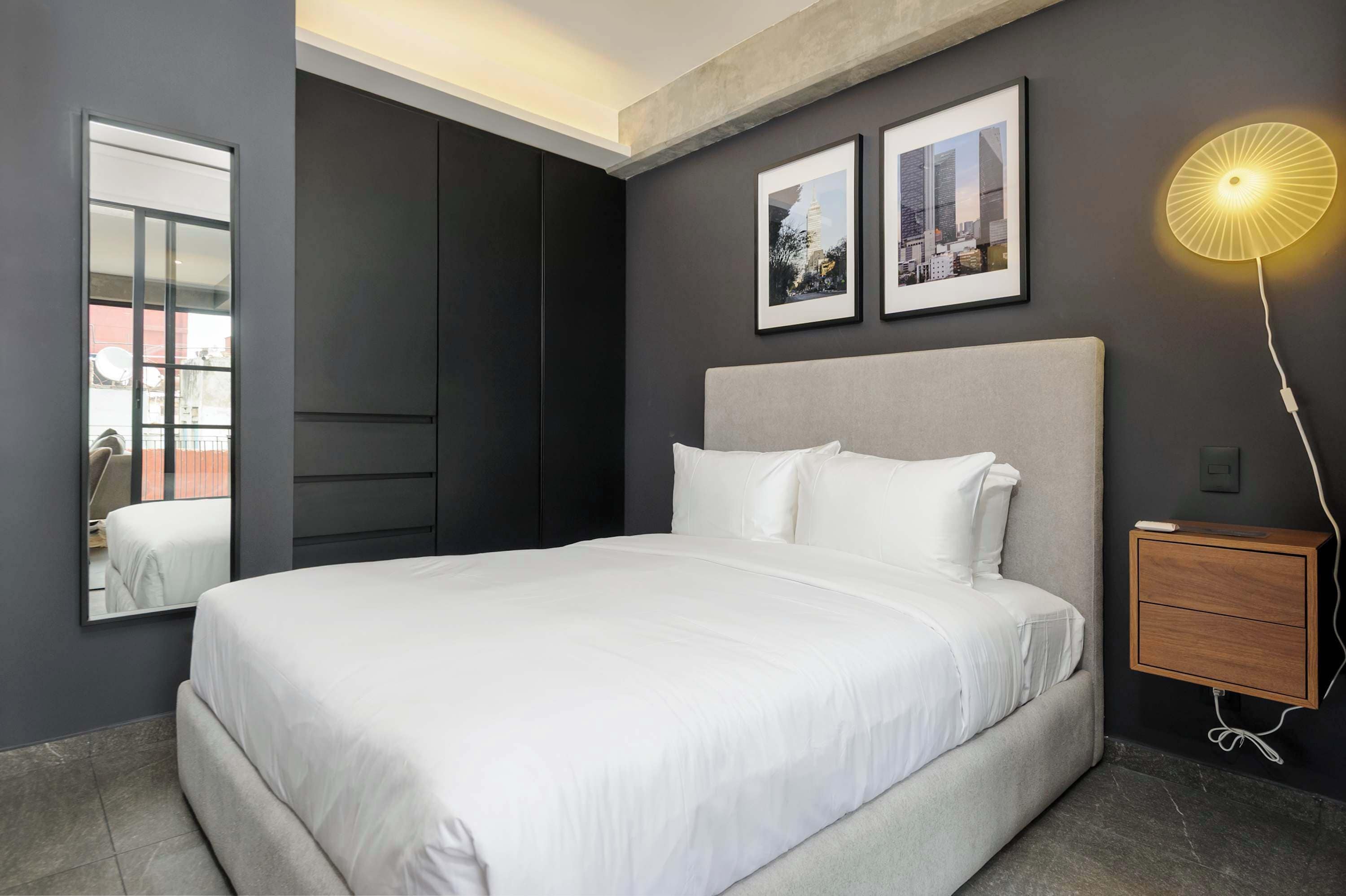 Une chambre moderne avec un grand lit, une armoire, une table de chevet et deux tableaux encadrés accrochés au mur.