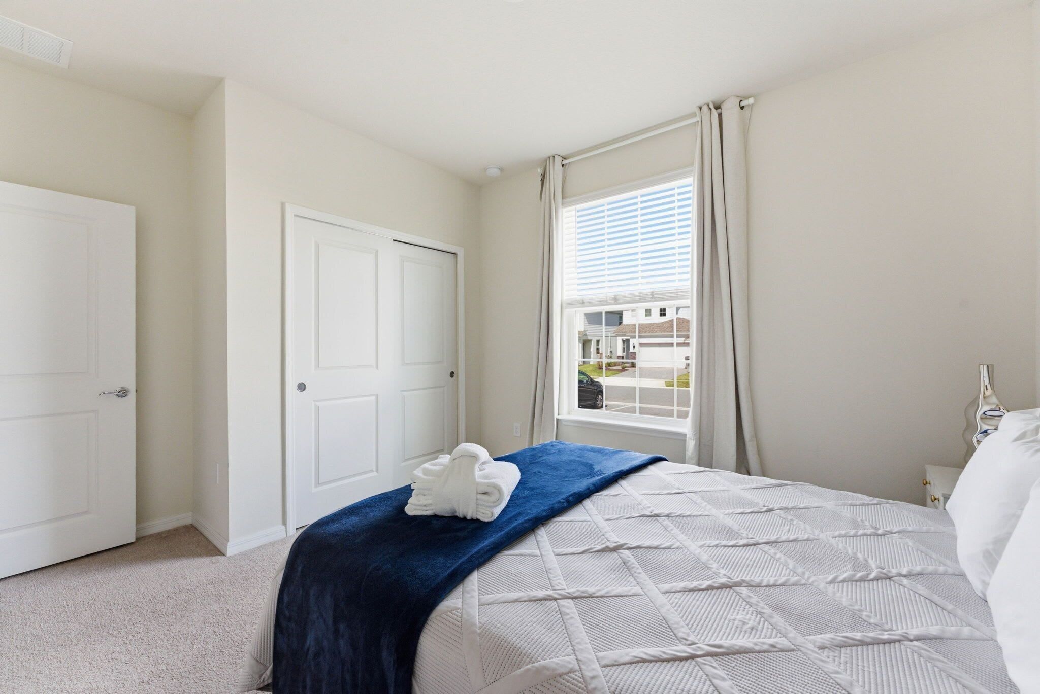 A bedroom with a bed, a window with curtains, a door, and a towel on the bed.