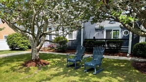 Un quartier résidentiel avec un arbre, deux fauteuils Adirondack et une maison à l’extérieur sombre.