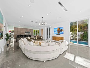 A modern living room with a curved sofa, a dining area, a kitchen, and a large TV. - Mid century modern perfection off Las Olas! (Fort Lauderdale)