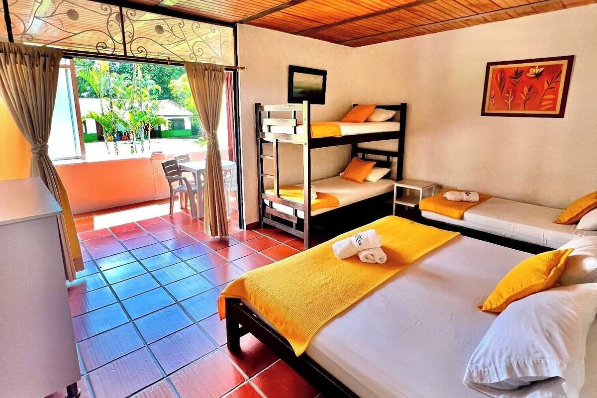 Quarto com cama, beliches, escrivaninha e vista para o verde lá fora.