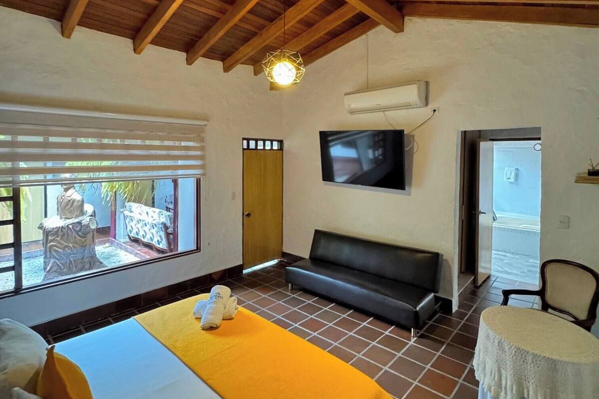 Quarto de hotel com uma cama, um sofá, uma televisão e uma pequena mesa.