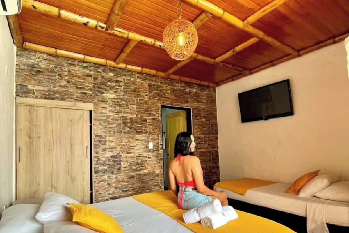 Quarto com uma cama, um guarda-roupa de madeira, uma parede de pedra, um candeeiro pendente e uma televisão na parede.