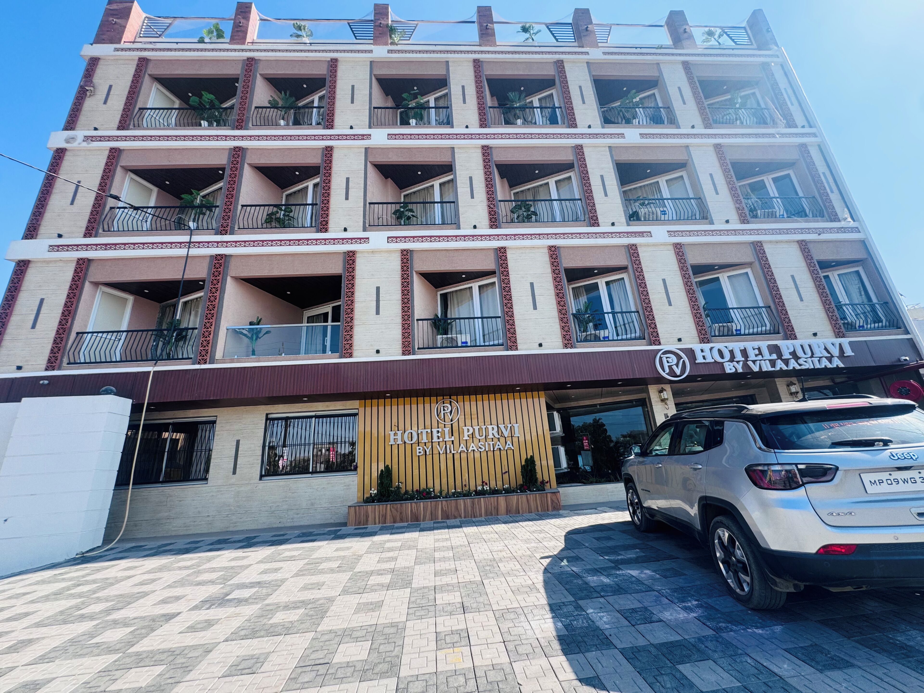 Un hotel de varios pisos con balcones, una entrada visible y un coche estacionado.