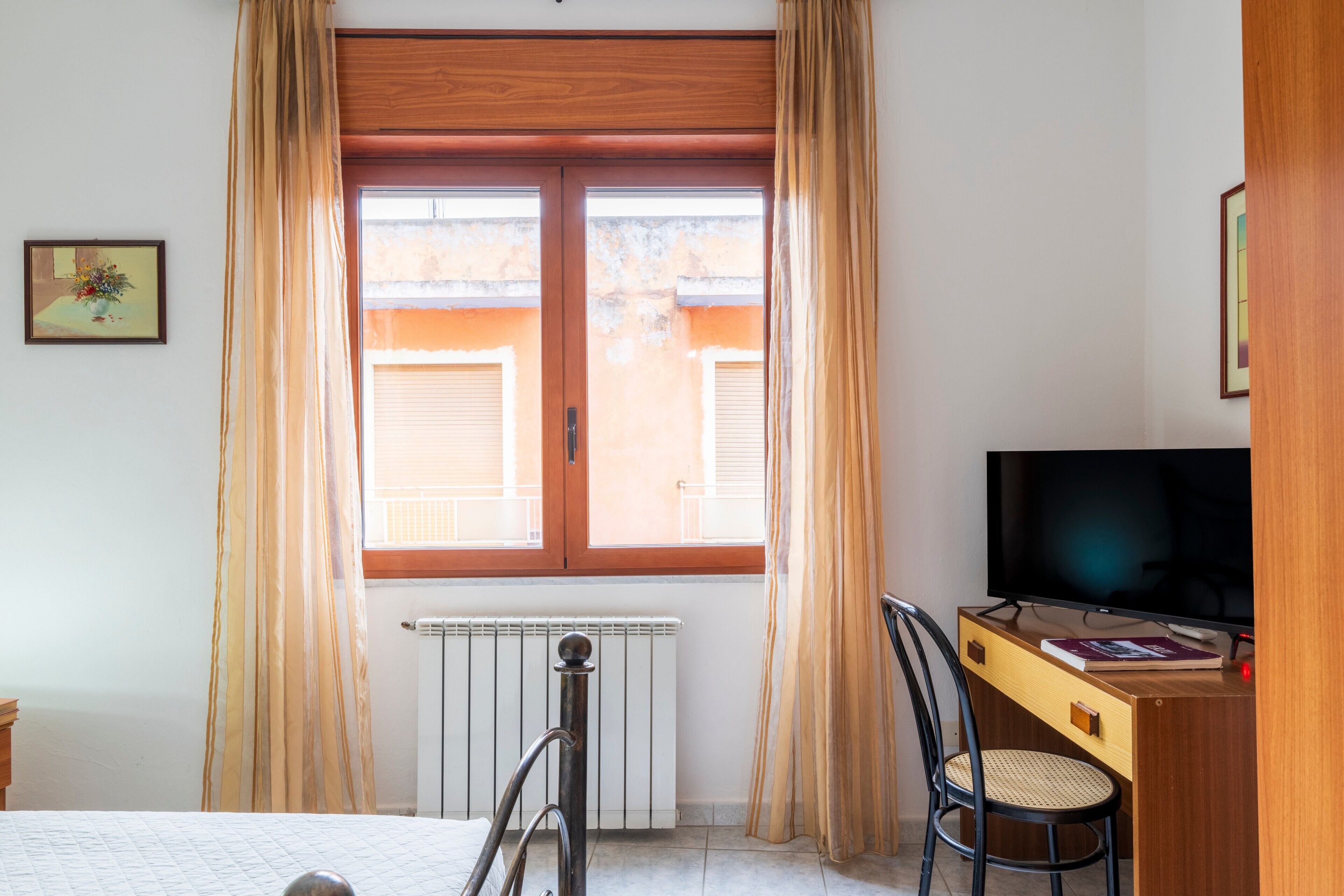 Una habitación de hotel con cama, escritorio con televisor, silla y ventana con cortinas.