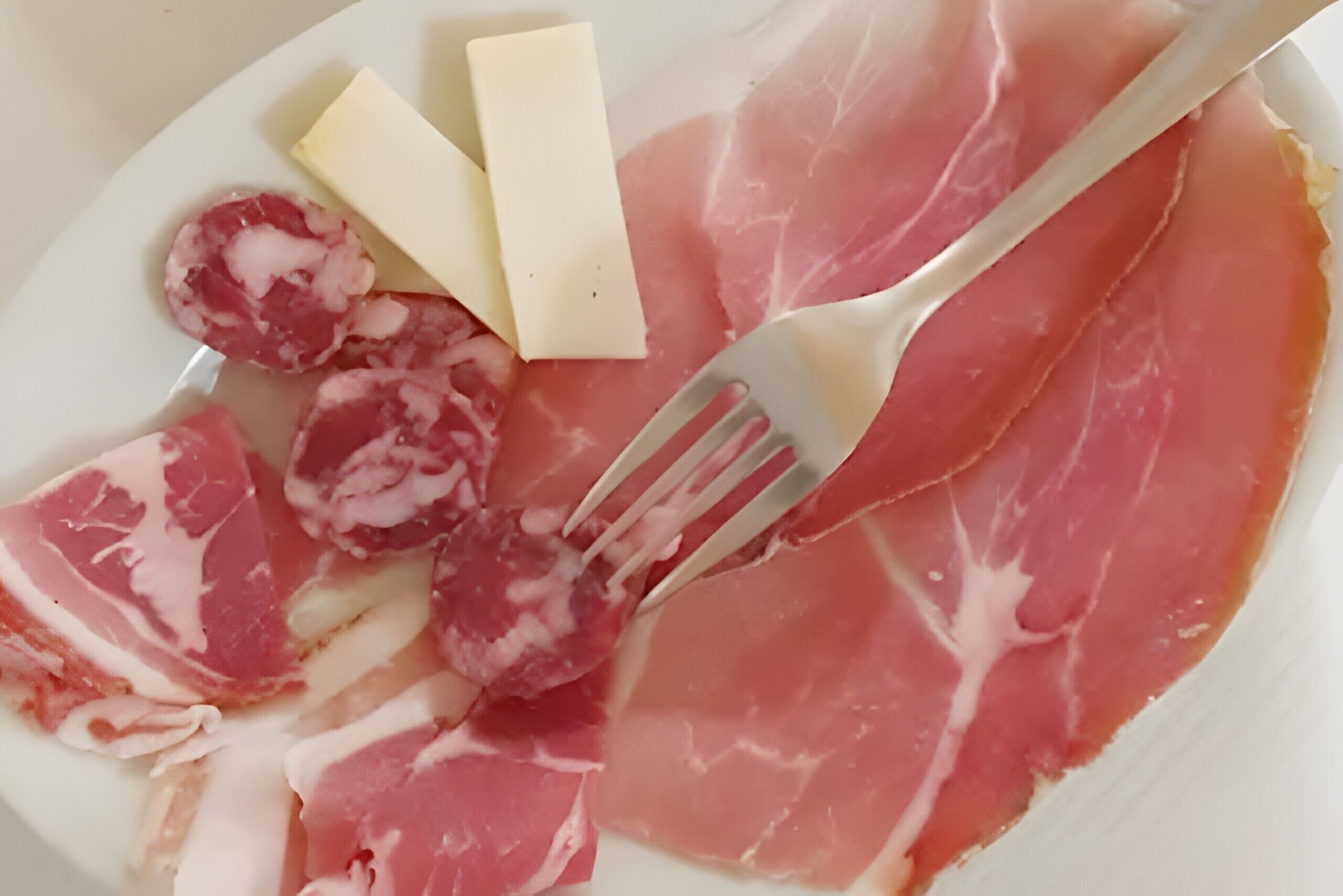 A plate with slices of cured meat, a fork, and a wedge of cheese.