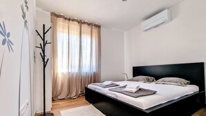 Ein modernes Schlafzimmer mit schwarzem Bettgestell, einer stehenden Stehlampe und einem großen Fenster mit transparenten Vorhängen.