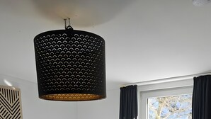 Habitación de hotel con una cama grande, una mesita de noche con lámpara, una lámpara colgante, una ventana con cortinas y vistas a árboles fuera.
