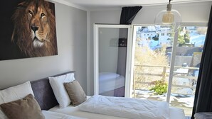 Ett hotellrum med två sängar, en stor målning av ett lejon, en balkong med utsikt och en hängande lampa.