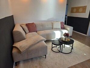 Un salon moderne avec un canapé d’angle, une petite table basse ronde et un vase décoratif.