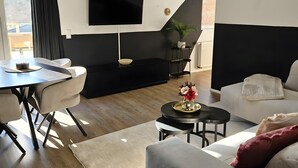 A modern living room with a dining area, a flat-screen TV mounted on the wall, a potted plant, and a staircase leading to an upper level. - Apartment 'Sauerland' with Mountain View, Balcony and Wi-Fi (Willingen (Upland))