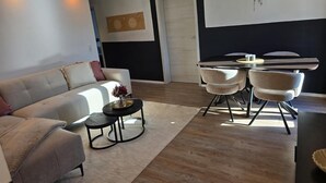 A modern living room with a sofa, a coffee table, and a dining area with chairs and a table. - Apartment 'Sauerland' with Mountain View, Balcony and Wi-Fi (Willingen (Upland))