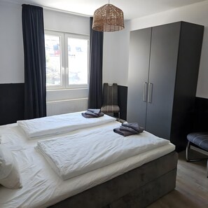 Une chambre avec deux lits, des rideaux foncés, un luminaire en matière tressée et une vue sur l’extérieur.