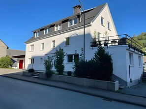 Ein zweigeschossiges Gebäude mit einer roten Tür, mehreren Fenstern und einem Balkon.