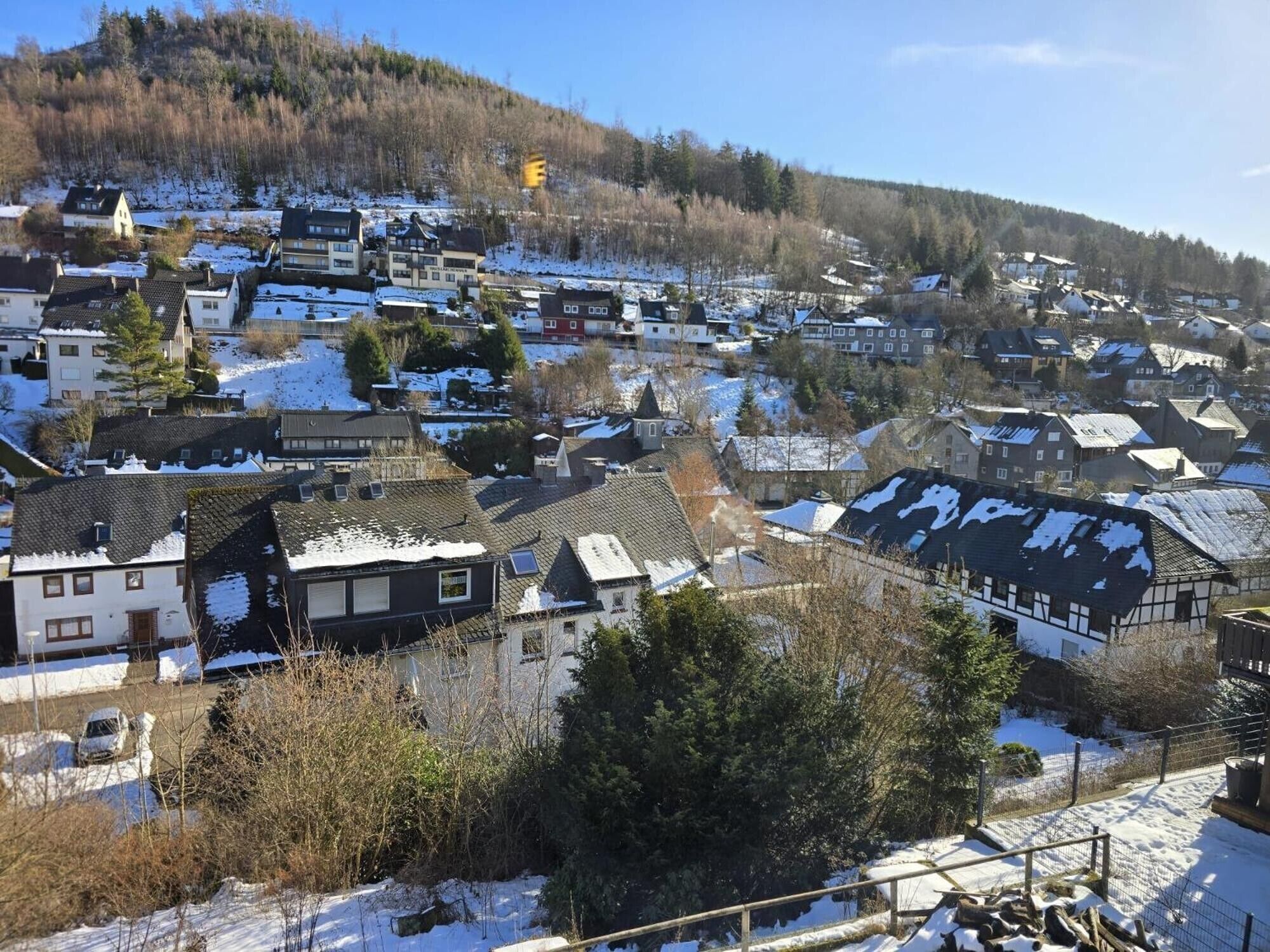 Un área residencial con casas, algunas con nieve en los techos, y una colina al fondo.