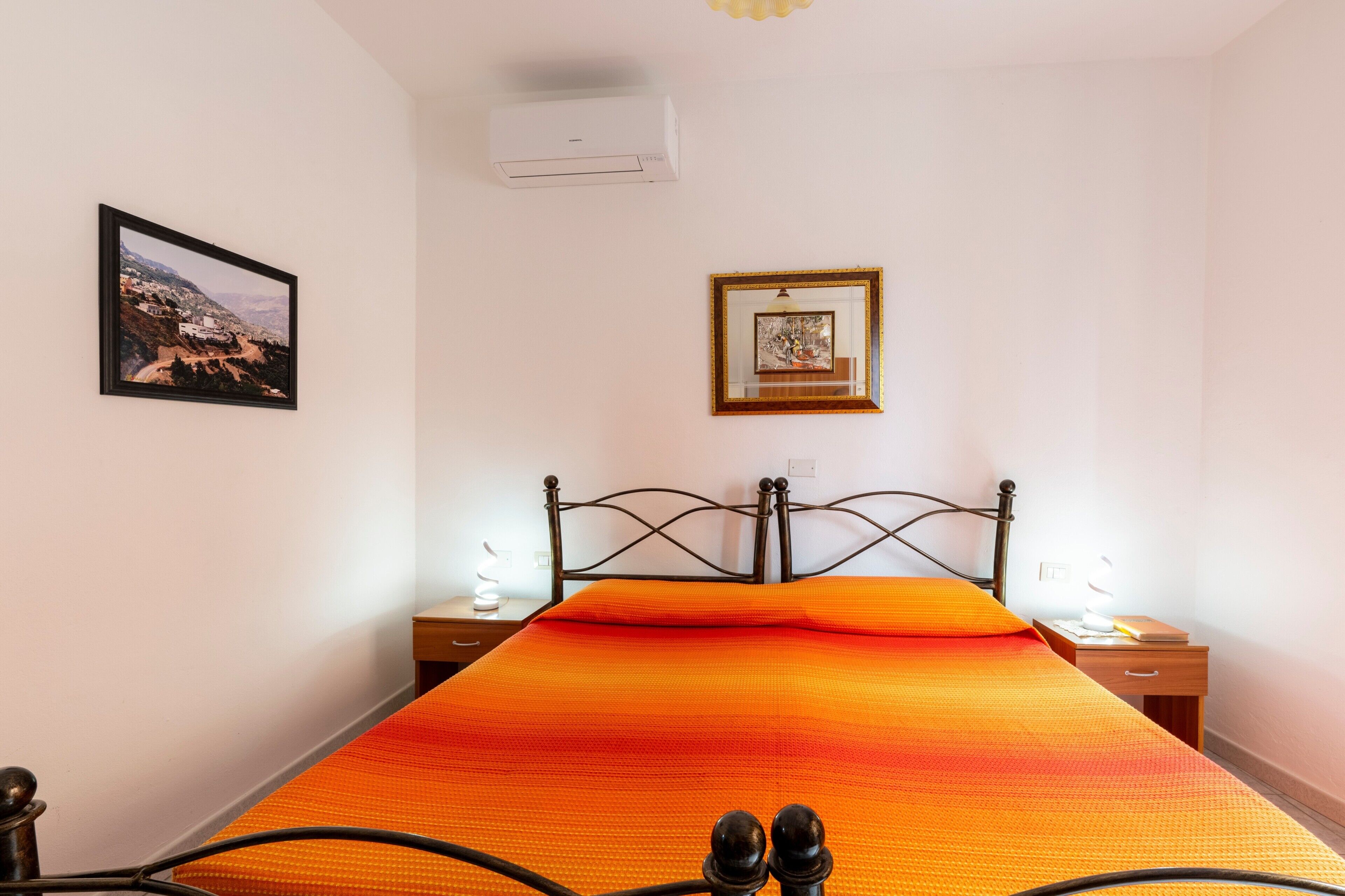 Un lit recouvert d’une couvre-lit orange, un tableau encadré accroché au mur et une table de chevet avec une lampe.
