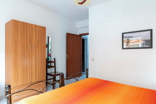 Una habitación con cama, armario de madera, silla y puerta que da a otra estancia.