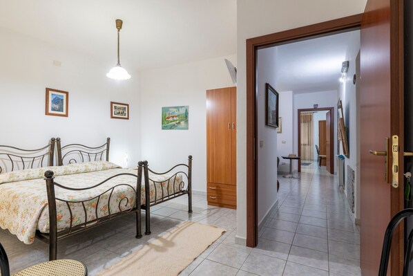A bedroom with a bed, a wooden wardrobe, a mirror, and a door leading to a hallway.