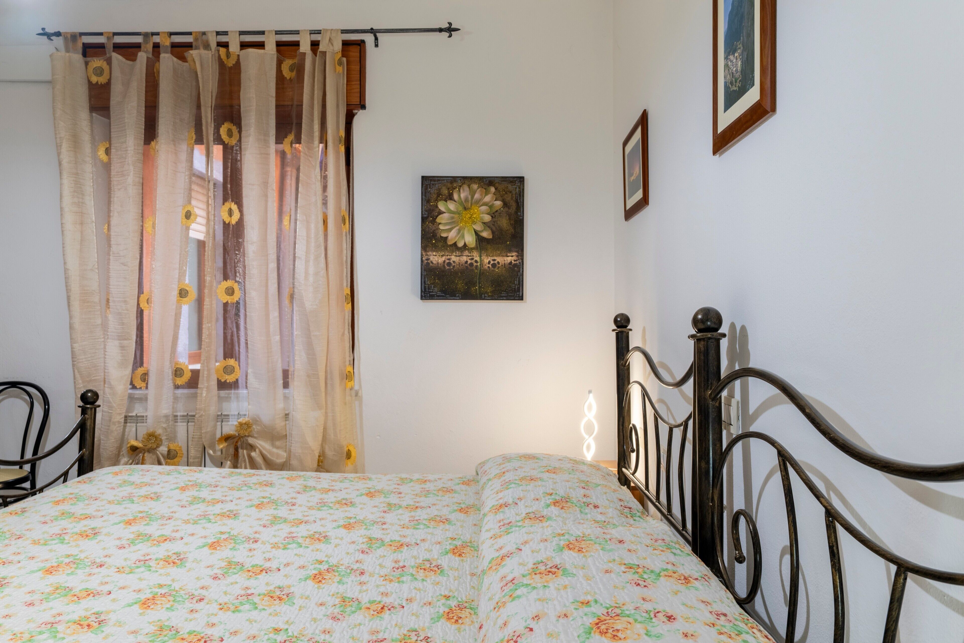 A bedroom with a bed, curtains, a wall-mounted picture, and a chair.