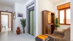 A living room with a sofa, a coffee table with books, a wooden cabinet, and a potted plant. - Double Room 205 with Air Conditioning (Jerzu)