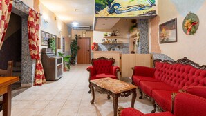 A spacious living area with a red sofa set, a wooden coffee table, and a dining table. There is a kitchen area with a counter and various kitchen items. - Double Room 205 with Air Conditioning (Jerzu)