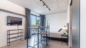 Ein modernes Hotelzimmer mit einem Bett, einem Schreibtisch mit zwei Stühlen, einem an der Wand befestigten Fernseher und einem großen Fenster mit Vorhängen.