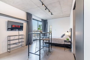 A modern hotel room with a bed, a desk with two chairs, a TV mounted on the wall, and a large window with curtains. - Soho Village en Palermo by Magno | 901 (Buenos Aires)