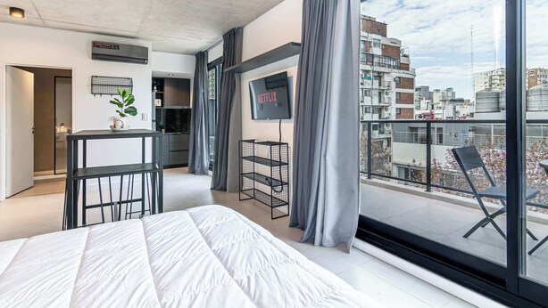 Ein modernes Hotelzimmer mit einem großen Bett, einem Fernseher, einem Balkon mit Sitzgelegenheit und Blick auf die Stadt.