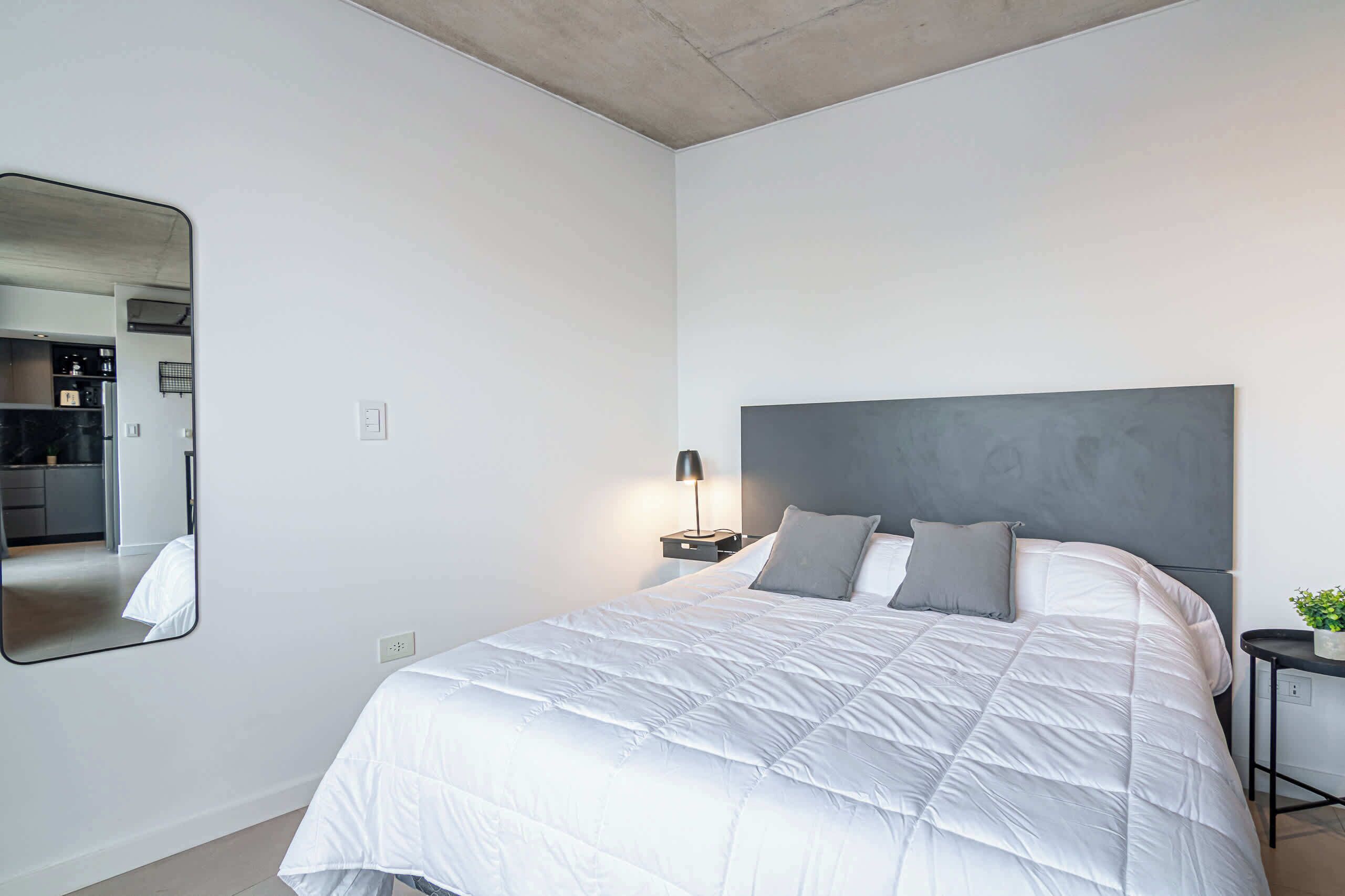 Um quarto moderno com uma cama grande, uma mesa de cabeceira, uma luminária e um espelho na parede.