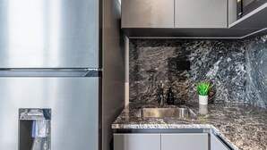 Eine Küche mit einem Edelstahlkühlschrank, einer Granit Arbeitsplatte, einer Spüle und einem kleinen Topfpflanzen.